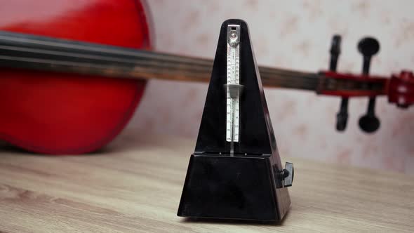 A black vintage metronome beats the rhythm while standing on the table, a cello is lying behind