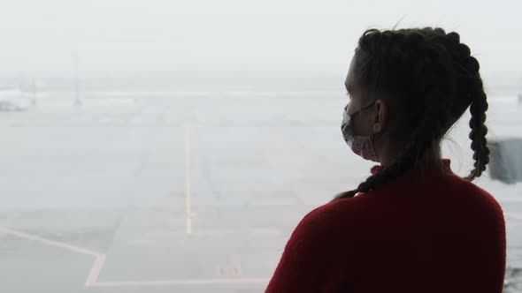 Silhouette of a Masked Young Woman at Airport Terminal Window Looking at Planes alt