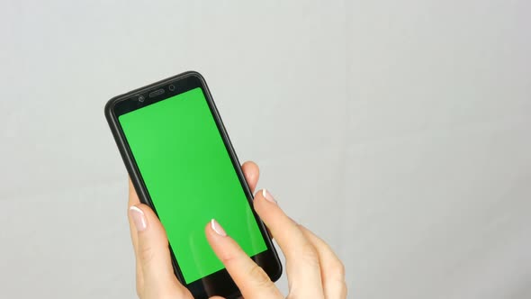 Wellgroomed Neat Female Hands with a Beautiful Manicure Hold a Black Smartphone with a Green Screen alt