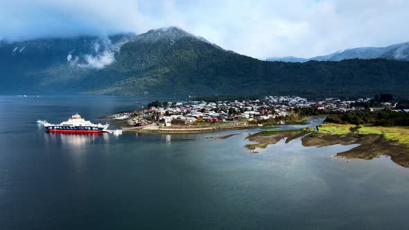 Aerial orbit of the coastline with a ferry in Hornopiren, Chile. Mountains with clouds in the backgr alt