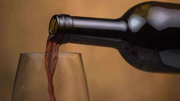 Pouring red wine into wineglass from wine bottle, background with warm colors and lights