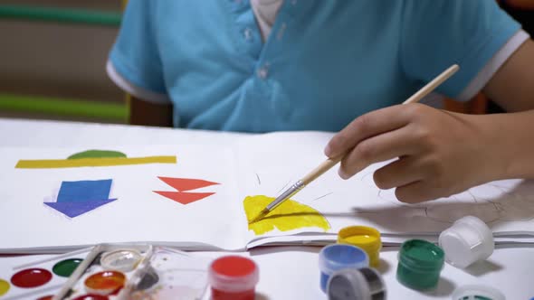 Child with a Brush in Hand Paints Sun with Yellow Paint on White Sheet of Paper