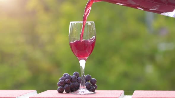 Homemade wine pouring into glass on green nature background