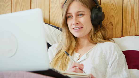 Young Woman with Headphones and Laptop in Bed