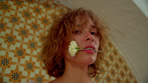 Portrait of a Darkhaired Woman with Wavy Hair with a Small Bouquet of Jasmine in Her Teeth Looking alt
