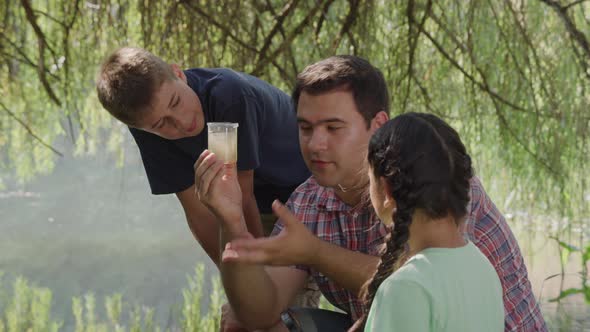 Kids at outdoor school look at cup of pond water with teacher