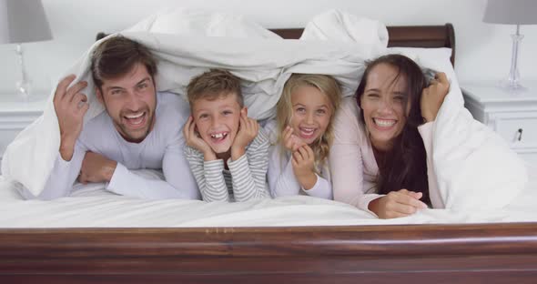 Family lying together under blanket in bedroom at home 4k alt