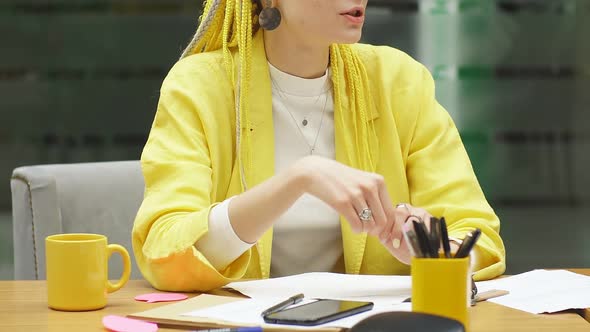 A Young Woman Dressed in a Yellow Jacket Sits at a Desk in the Office and Discusses Working Moments