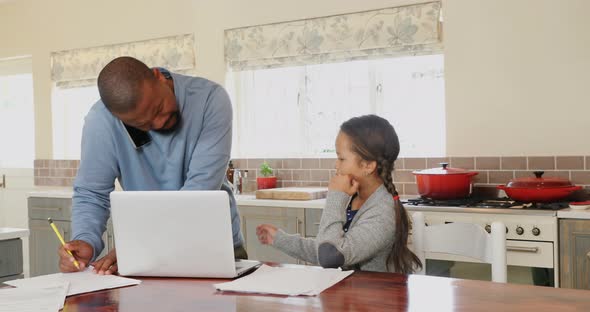 Father talking on mobile phone while daughter sitting beside in kitchen alt