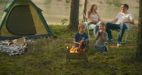 A Family in Nature, Parents Watch As Two Boys at the Fire Roast Marshmallows on Sticks in the alt