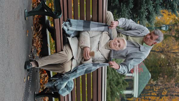 Vertical View of Happy Senior Retired Grandparents Sit on Bench in Autumn Park Talk Casually Drink alt