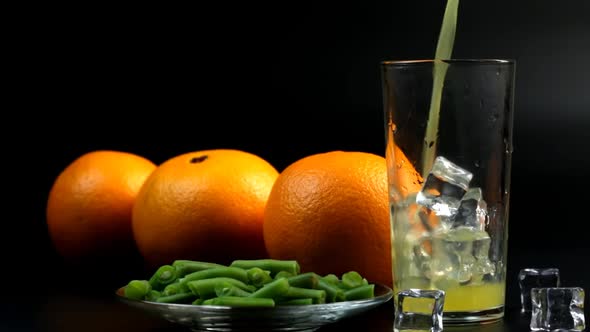In A Tall Glass With Ice, Pour Orange Juice And Three Oranges Nearby And Beans