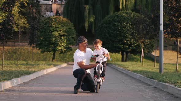 Dad Teaching Son To Drive a Bike in the Summer Park alt