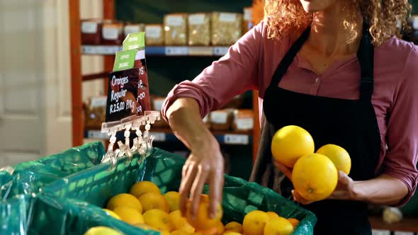 Smiling female staff arraigning sweet lime in crate at organic section alt