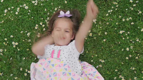 Little Happy Child Girl in Dress with Bow on Head Laying on Green Lawn in the Park