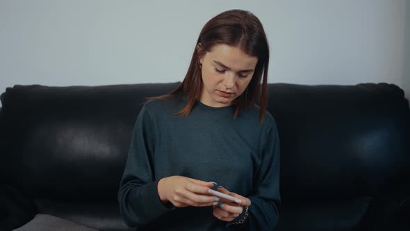 The Redhaired Freckled Focused Young Woman is Playing on the Phone Sitting on the Black Sofa at Home alt