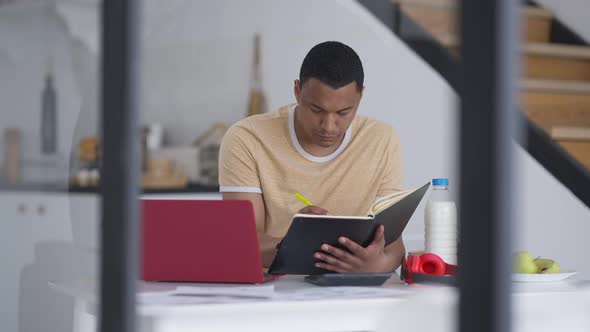 Serious Young Professional Writing with Pen in Sketchpad and Typing on Laptop Keyboard in Slow alt