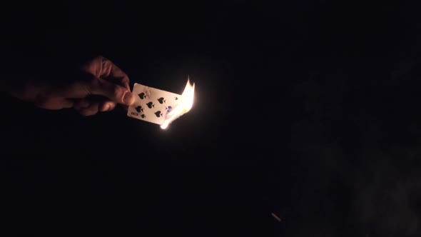 Hand Holds Burning Card on Black Background Near Campfire on Nature. Slow Motion alt