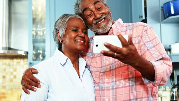 Senior couple taking selfie from mobile phone in kitchen alt