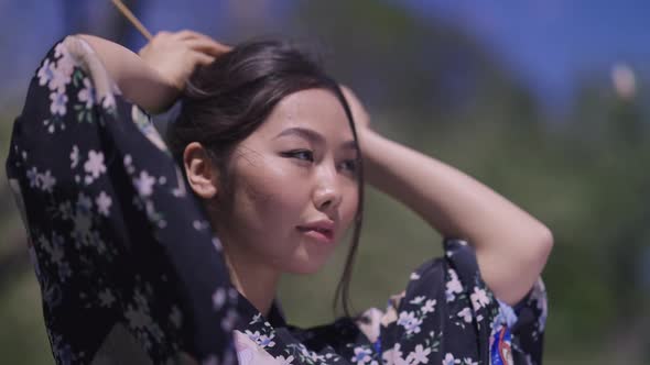 Gorgeous Asian Slim Young Woman Making Buntail Standing in Sunlight in Spring Park Looking Away alt