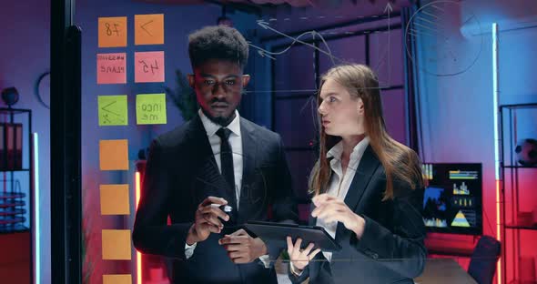 Businessman with Pretty Concentrated European Female Colleague Working Together Near Glass Wall alt