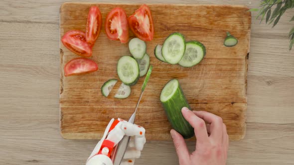 Man with Robotic Prosthetics Hand with Knife on It Is Trying To Cut Cucumber for Slices on Wooden alt