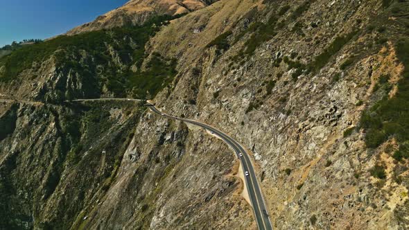 Aerial view of a road running between a mountain and the ocean alt