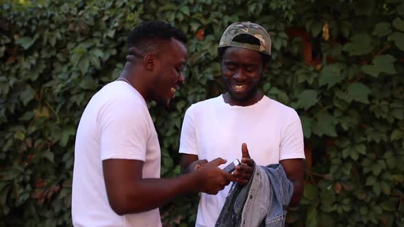 Two African Guys Laugh and Show Something To Each Other on the Phone