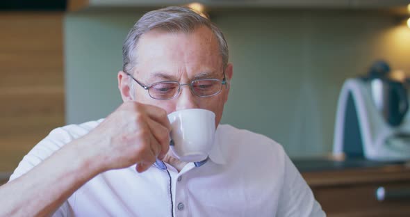 Delicious Drink Pleasant Elderly Man in Spectacles Sitting on Chair in Kitchen alt