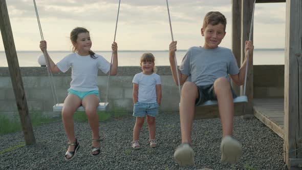 Children Swing on a Swing in the Street at Sunset. alt