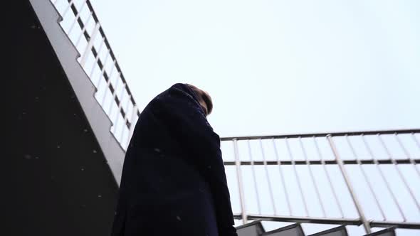 Sad Young Businessman Stands and Look Down Under Snowfall alt