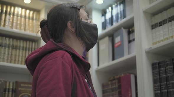 Woman Wearing Glasses and Mask Against Virus Chooses Book to Buy at Bookstore