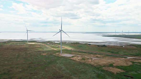 Drone Flying Straight on Wind Turbine Cloudy Sky and Lake on Background alt