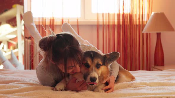Closeup Portrait of Pleased Woman Lying on Bed at Home with Her Loved Dog Welsh Corgi alt