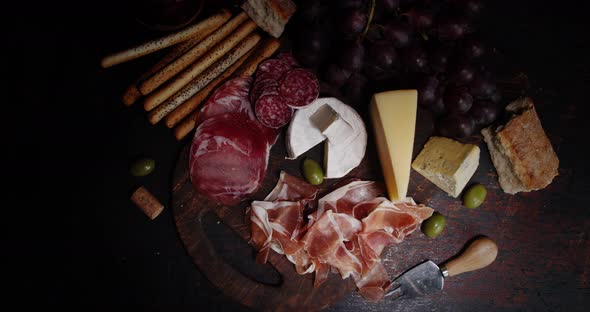 Antipasto with Grapes Slowly Rotates on a Cutting Board.  alt