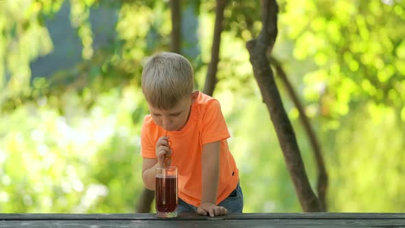 Portrait of a little boy. A child sits at a table in the Park and drinks juice through a straw.