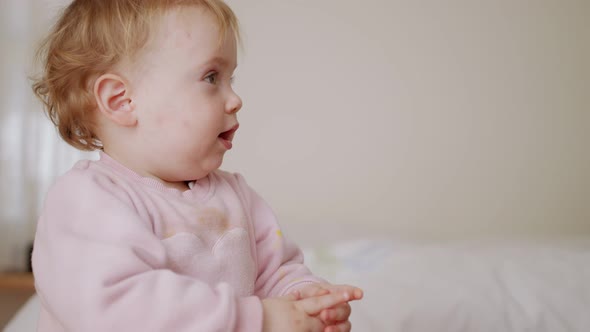 Cute baby sitting on a bed, playing, rolling and laughing alt