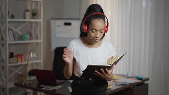 Positive Creative Young African American Woman in Headphones Dancing to Playlist Writing in alt