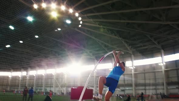 Pole Vault Training in the Stadium - a Young Man in Blue Shirt Jumping Over the Bar alt