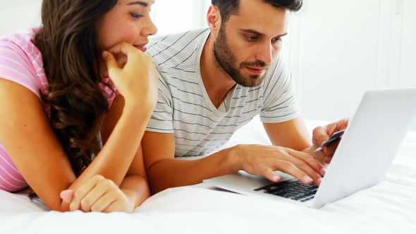 Couple doing online shopping on laptop in bedroom alt