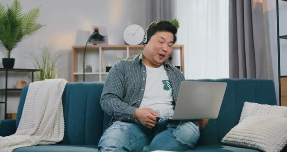 Asian Guy in Headset Enjoying His Video Call while Sitting on Comfortable Sofa alt