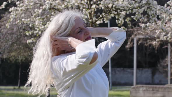 Mature woman touching her hair in blossoming spring park alt