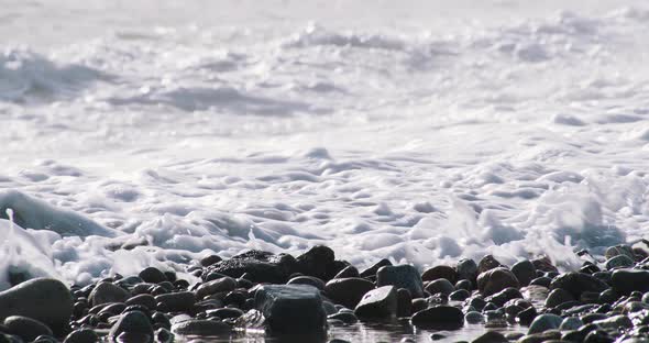 60FPS: Waves crash on a stone beach in Barcelona creating beautiful reflections - zoomed shot alt
