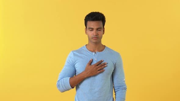 Portrait of religious young Indian man praying with faith against yellow background