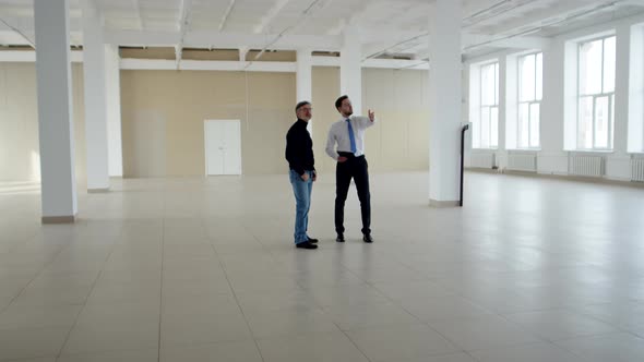 Realtor and Businessman Stand in Middle of an Empty Room and Inspect It Front View alt