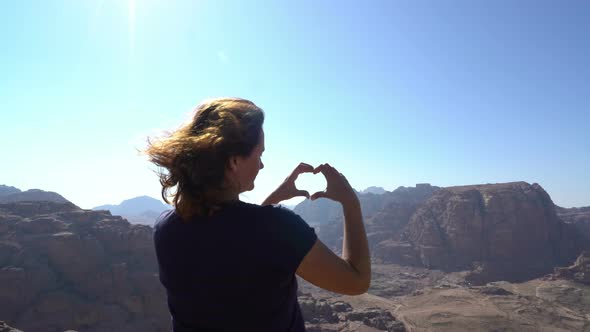 Woman traveller standing at the edge of mountains and showing love sign