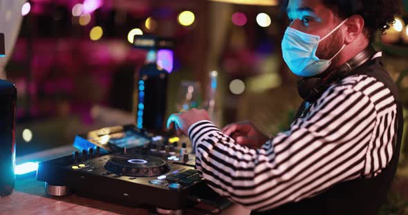 Dj mixing outdoor at cocktail bar - African young man mixing music while wearing safety mask alt
