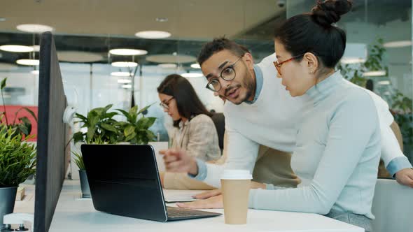 Colleagues Talking Looking at Laptop Screen Working with Computer in Shared Office alt