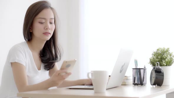 Beautiful young freelance asian woman smiling working on laptop computer and talking smart phone. alt