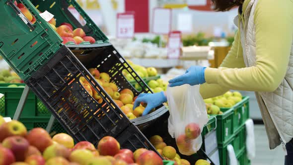Shopper in medical gloves picking apples from plastic boxes at grocery store alt